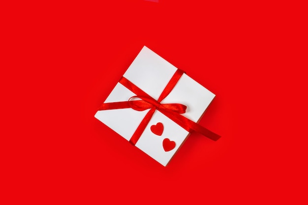 Подарок на день святого валентина с бумажными красными сердечками на красном фоне