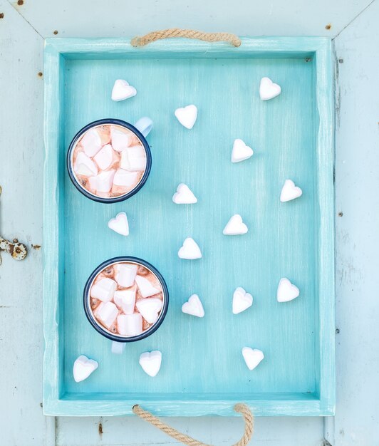 Saint Valentine's vakantie groet set. Warme chocolademelk en hartvormige marshmallows in oude emailmokken op turquoise dienblad over blauwe houten
