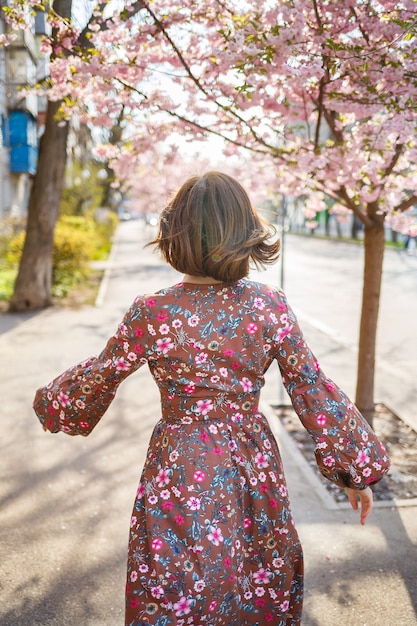 さくらは街の通りの木に花を咲かせて枝分かれしています。桜が咲く通りで回転する幸せな女の女の子。さくらの花。