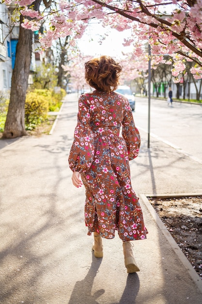 Sakura branches with flowers on a tree in the streets of the city. Happy woman girl spinning on the street with blooming sakura. Sakura blossoms.