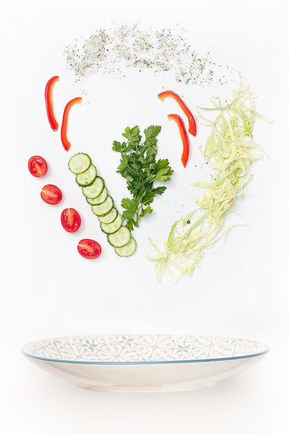 The salad bowl in flight with vegetables: tomato, pepper, cucumber, cabbage on white studio background