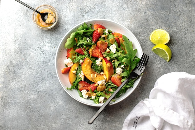 Photo salad bowl with arugula, strawberry, cottage cheese, nectarine and peanut paste. healthy eating concept