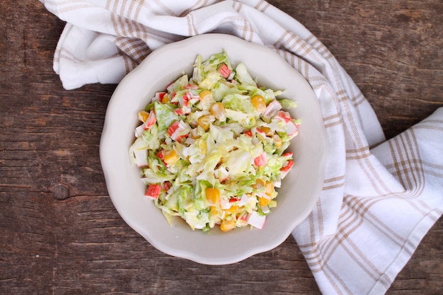 Salad of cabbage with grains corn and crab sticks in a plate on an old background Top view
