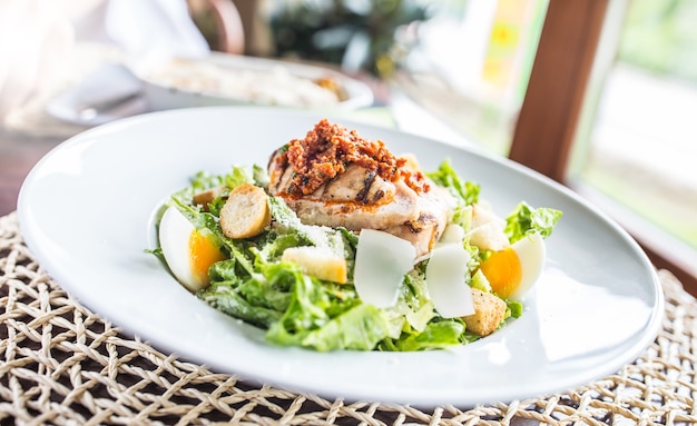 Salad caesar with grilled pieces of chicken breasts on white plate in restaurant.