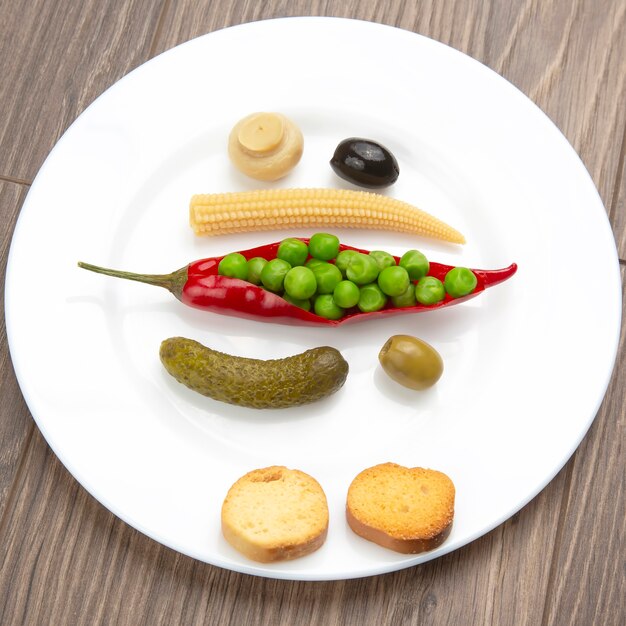 Salad of canned and pickled olives, mushrooms, corn, peas, cucumber and red pepper on a white plate.  