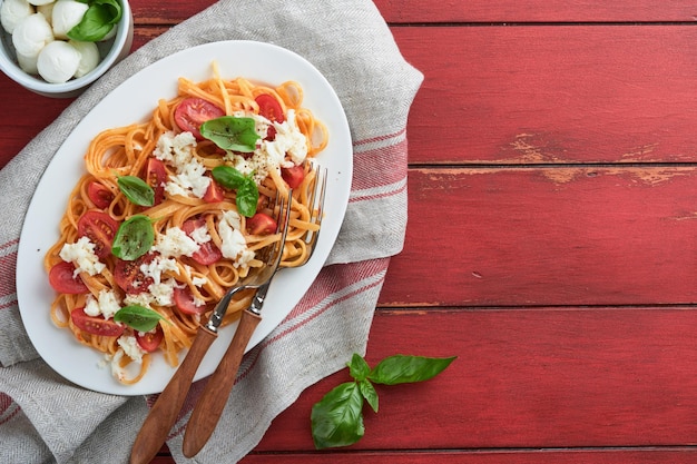 赤い素朴な木の背景に白い皿にバジルとモッツァレラチーズで割ったサラダ・カプリまたはパスタ・スパゲッティ・アラ・カプリ伝統的なイタリア料理イタリア料理のコンセプトトップビュー