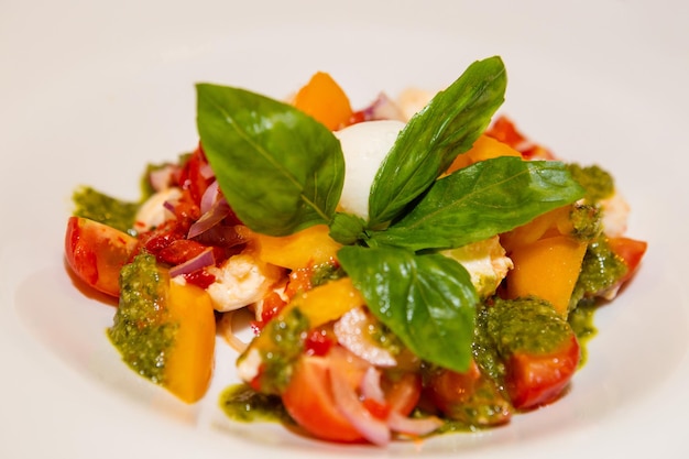 Salad Caprese served with pesto and basil leaves in white plate Salad with tomato caprese basil and pesto