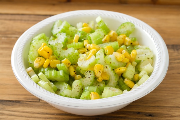 Salad celery with corn in white bowl on brown 