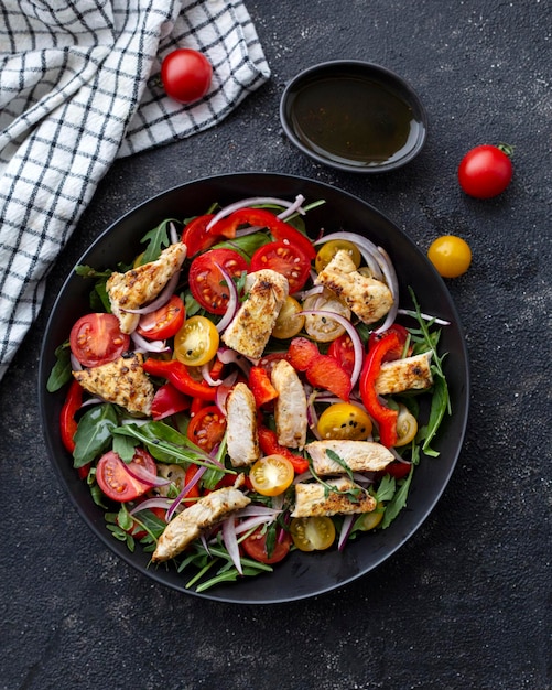 Salad of cherry tomatoes arugula and grilled turkey on a dark background
