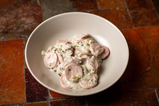 Salad of chopped sausages greens and sour cream Simple meat salad on plate on stone background