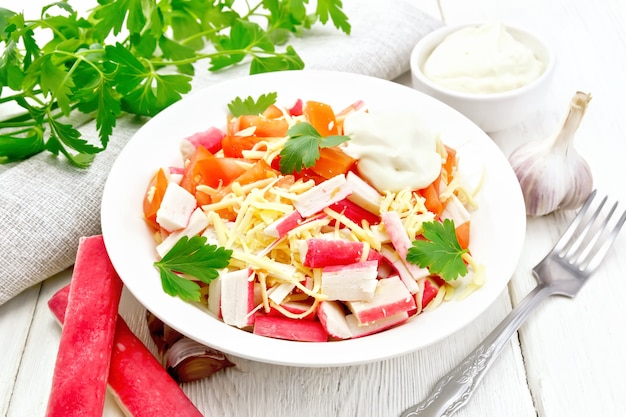 Salad of crab sticks, cheese, garlic, tomatoes and mayonnaise, kitchen towel, parsley on a wooden board background