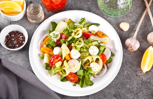 Salad of fresh cherry tomatoes, mozzarella, basil and other greens on the dinner table. Top view.