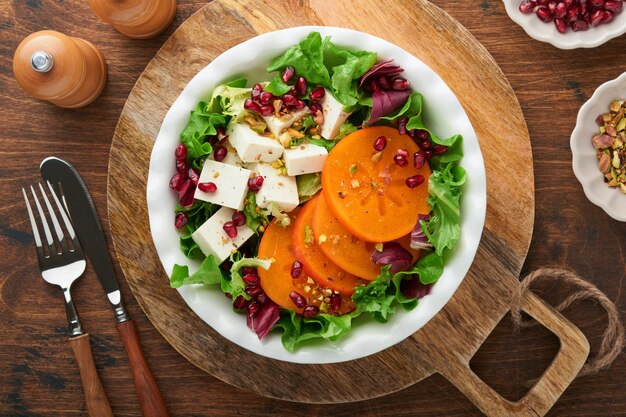 Salad Fresh green salad with feta cheese persimmon pomegranate and pistachio on white plate Idea for healthy delicious winter Christmas salad Healthy balanced eating Top view