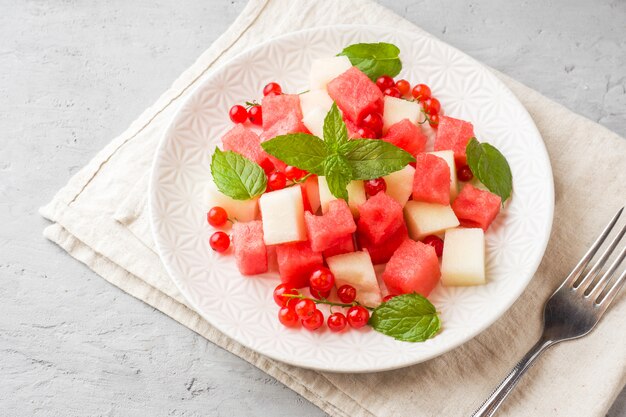 Salad of fresh juicy pieces of watermelon, melon, red currant and mint leaves on a plate