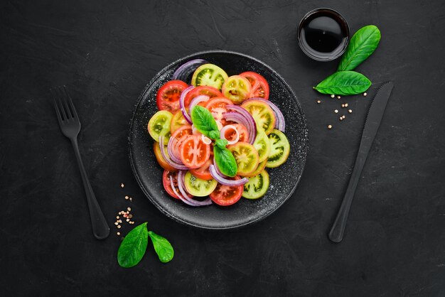 Salad of fresh tomatoes and onion in a black plate On the old background Top view Free space for your text