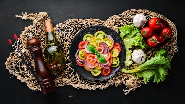 Salad of fresh tomatoes and onion in a black plate On the old background Top view Free space for your text