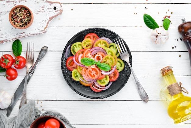 Salad of fresh tomatoes and onion in a black plate On the old background Top view Free space for your text