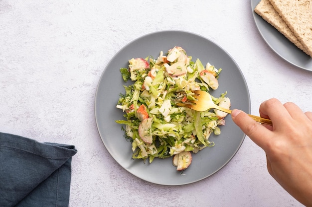 Salad of fresh vegetables and crab sticks in a plate with female hand The concept of healthy eating