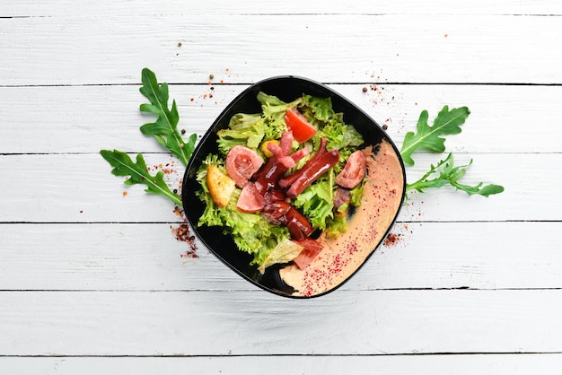 Photo salad of fresh vegetables and sausages in a black plate on a wooden background top view free space for your text