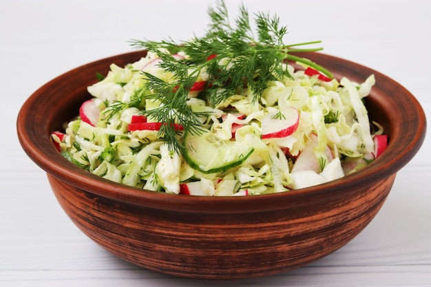 Photo salad from fresh vegetables: cabbage, radish, cucumber, onion and dill, in a brown salad bowl