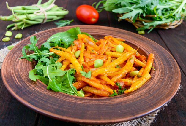 Salad from green beans, stewed with onions in tomato sauce and green leaves of arugula in a ceramic bowl