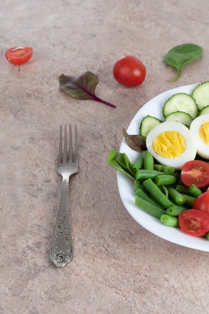 Salad of green vegetables, tomato and rice in a white plate. Rice with vegetables and eggs on a white plate.