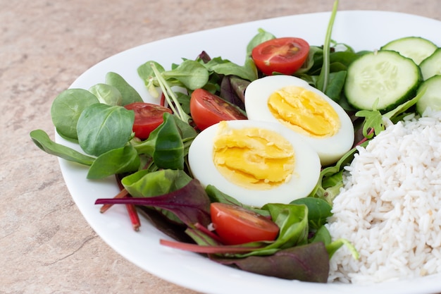 Salad of green vegetables, tomato and rice in a white plate. Rice with vegetables and eggs on a white plate.