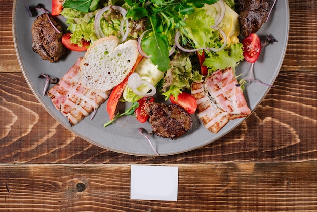 A salad of grilled meat, bacon and vegetables on wooden background