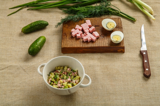 Salad ingredients in a bowl and over cutting boards on beige fabric background