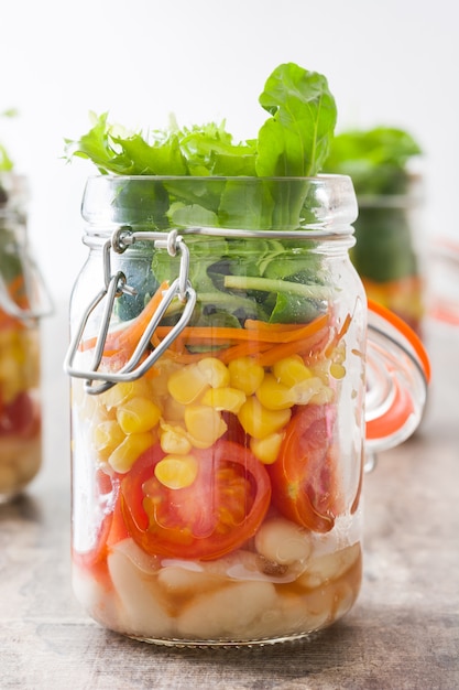 Salad in jar with fresh vegetables on wooden table