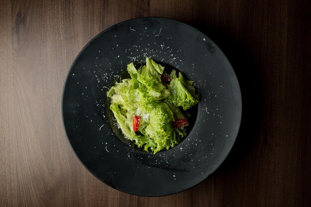 Salad of lettuce chili peppers parmesan cheese in a black plate Salad in a black plate