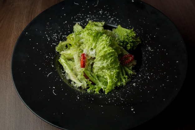 Salad of lettuce chili peppers parmesan cheese in a black plate Salad in a black plate