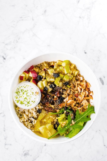 Salad lunch bowl with mix salad, chicken breast, apple, pineapple, raising, dates, brown rice and walnut. Keto salad in bowl on marble.