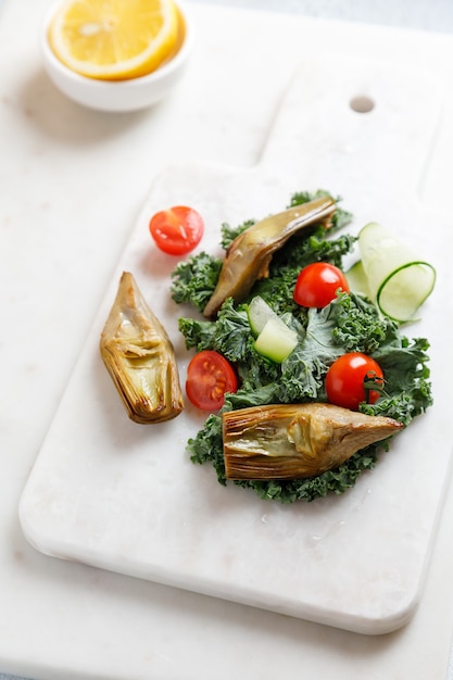 salad on a marble board with baked artichokes cale cucumber and cherry