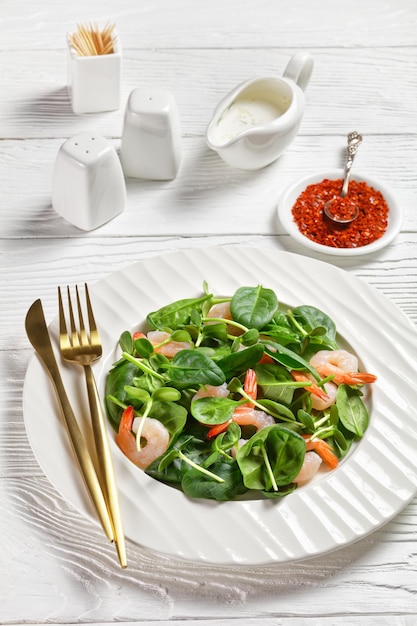 Salad of microgreens with avocado shrimps, baby spinach leaves, fresh sunflower sprouts, yogurt and tahini dressing with chili flakes served on a white plate on a white wooden background, top view