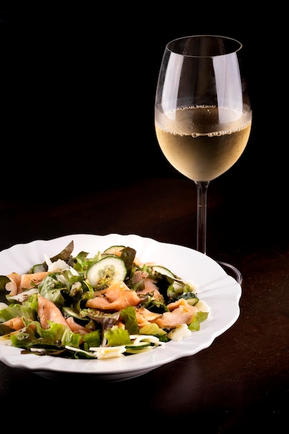 木製のテーブルにキュウリとサーモンのサラダ プレート健康的な食事白緑ワインのクローズ アップのガラス