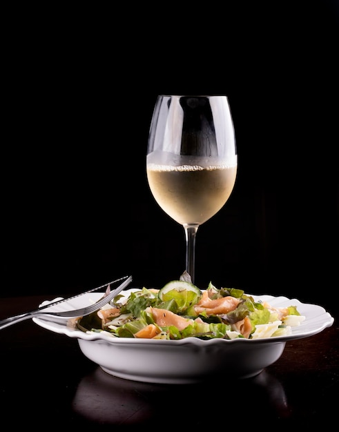 Salad plates with cucumber and salmon on wooden table healthy eating with glass of white green wine from the front with fork and knife