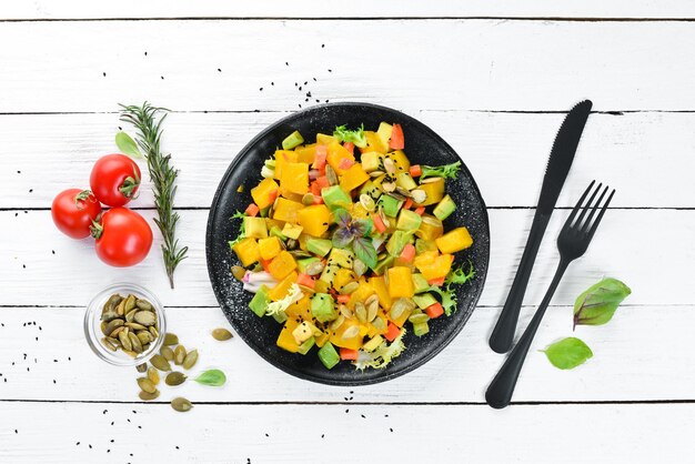 Salad of pumpkin avocado and pumpkin seeds On a white wooden background Top view Free space for your text