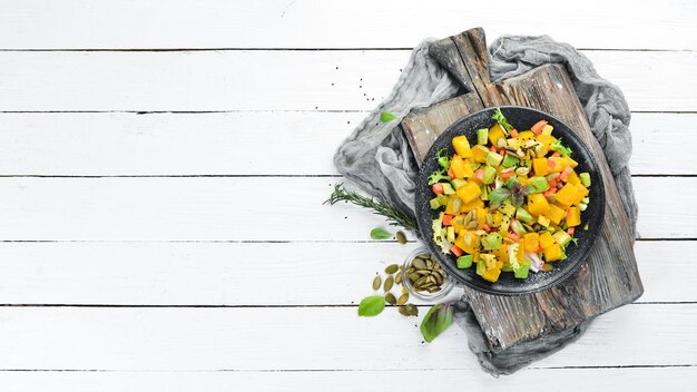 Salad of pumpkin avocado and pumpkin seeds On a white wooden background Top view Free space for your text