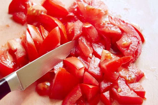 Insalata di pomodori succosi rossi maturi in una tavola di legno durante il processo di cottura.