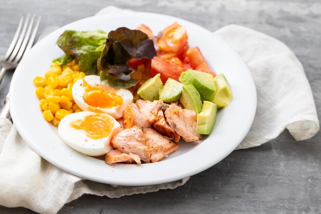 Салат из лосося с овощами и вареным яйцом на белой тарелке на керамике