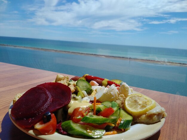 Foto insalata servita in piatto su tavola contro il mare