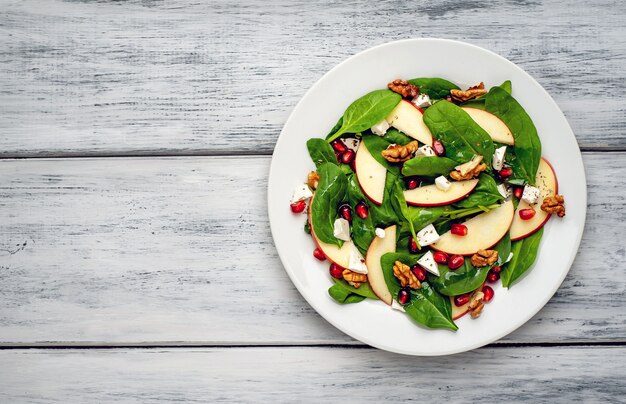 Salad of spinach, apples, pomegranate, cheese, walnuts on a wood background