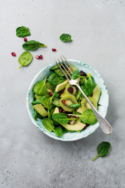 Salad of spinach baby leaves, watercress, kiwi, avocado and pomegranate in an old ceramic plate on a gray concrete surface. Selective focus. Top view. Copy space