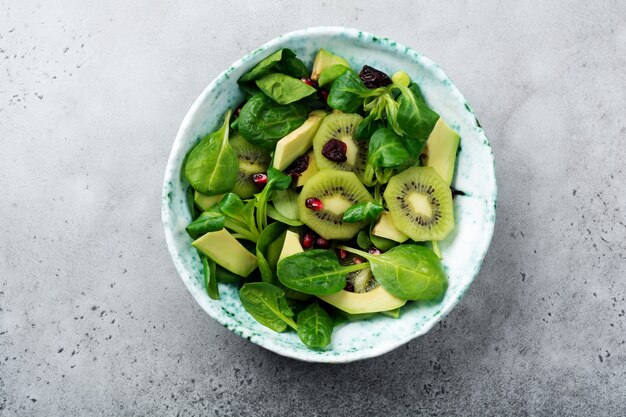 Salad of spinach baby leaves, watercress, kiwi, avocado and pomegranate in an old ceramic plate on a gray concrete surface