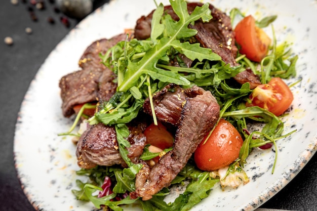 Salad of steak arugula and cherry tomatoes on a dark background