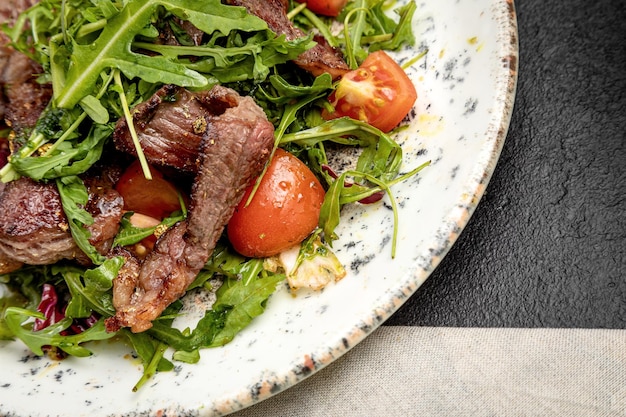 Foto insalata di bistecca di rucola e pomodorini su fondo scuro