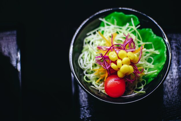 Salad of vegetables with yellow corn on a black saucer