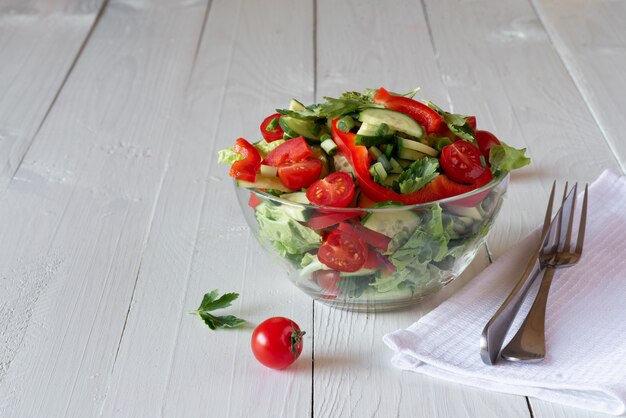 Салат на белой деревянной предпосылке от томатов, огурца, салата и красного перца. Концепция здорового питания.