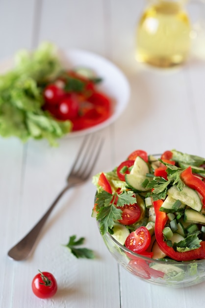 Insalata su un fondo di legno bianco da pomodori, cetrioli, lattuga e peperone. concetto di mangiare sano.